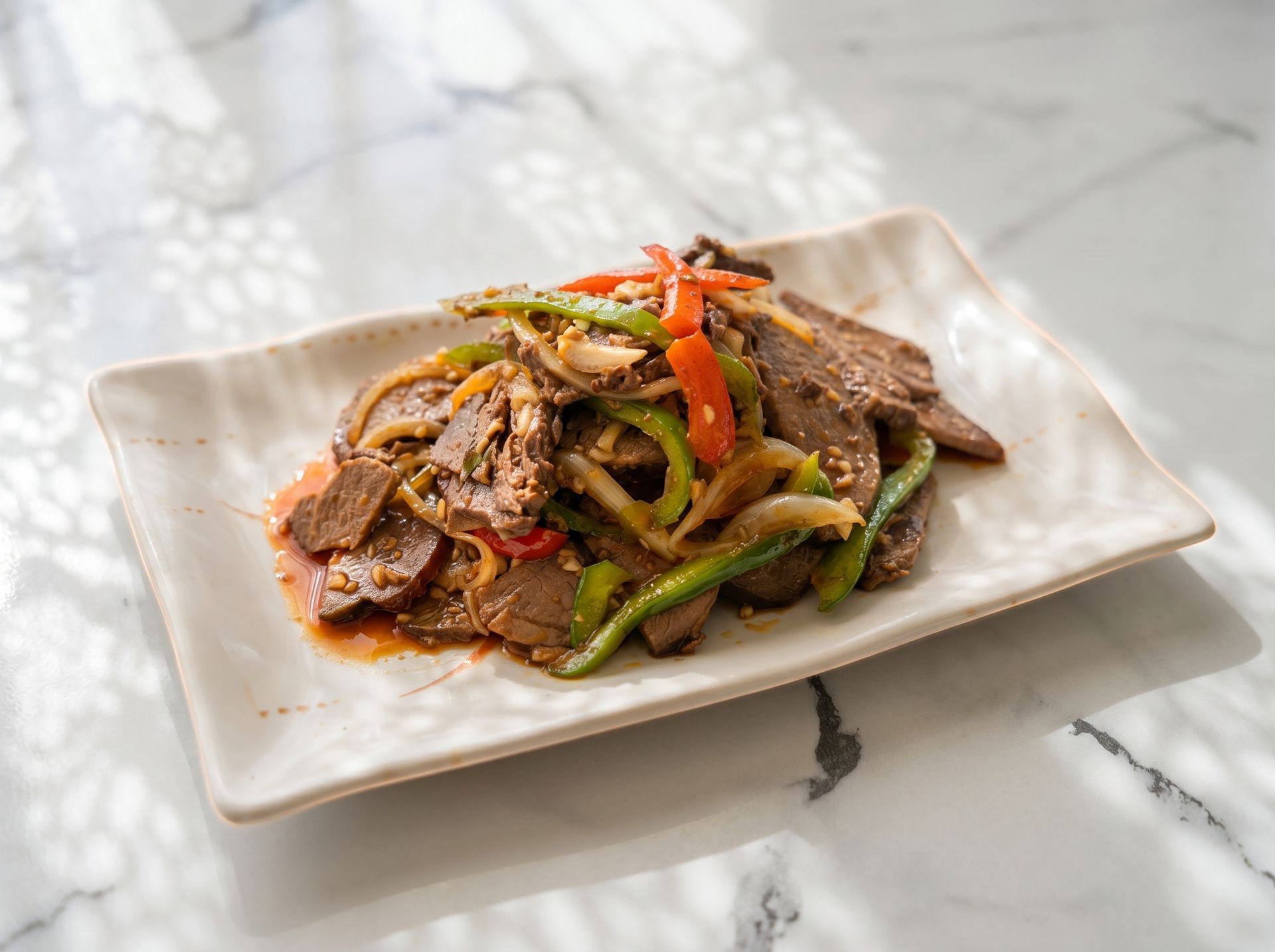 Stir-fried beef and vegetables on a white square plate, garnished with red and green peppers.
