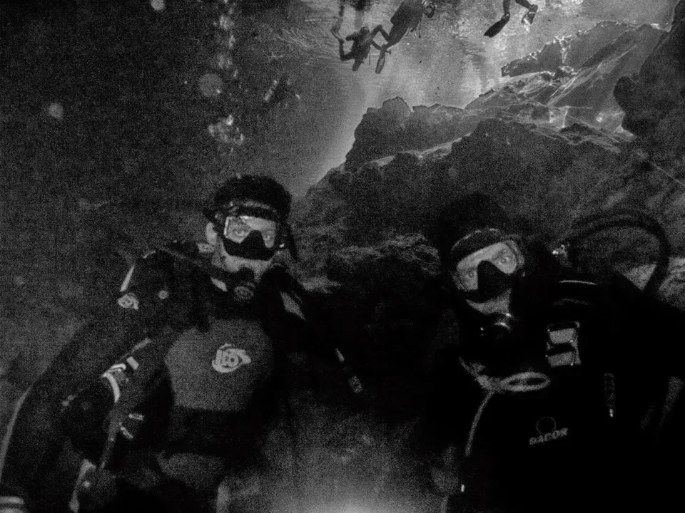 Three scuba divers underwater near a rocky cave, wearing masks and dive gear.