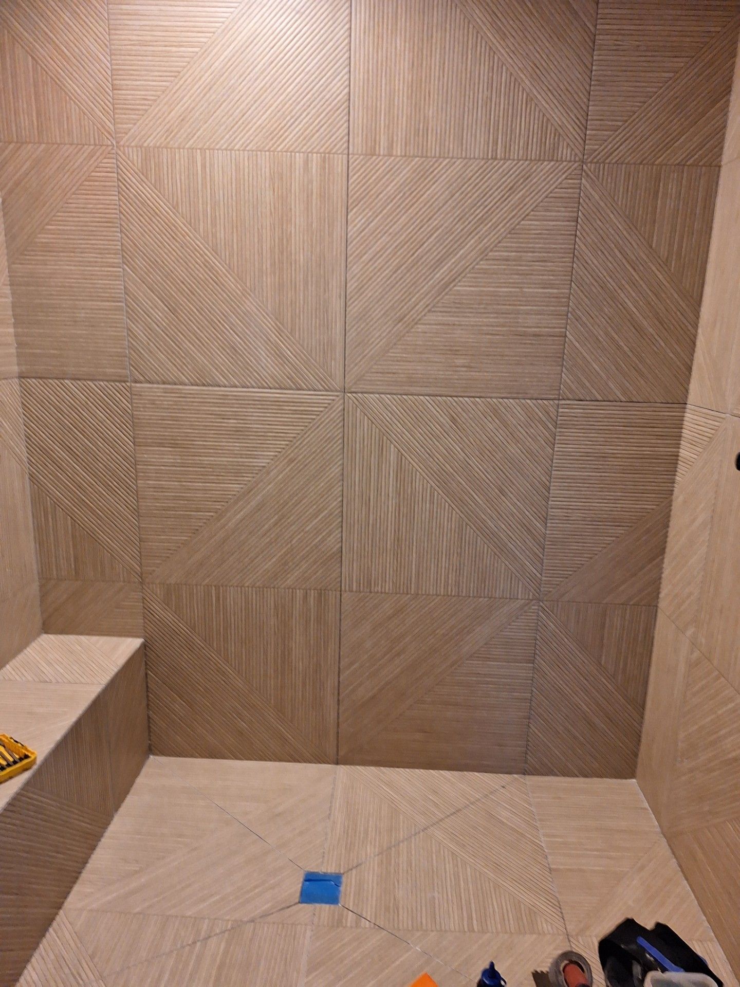 Person installing gray carpet tiles on a wood floor, holding a tile, measuring tape nearby.