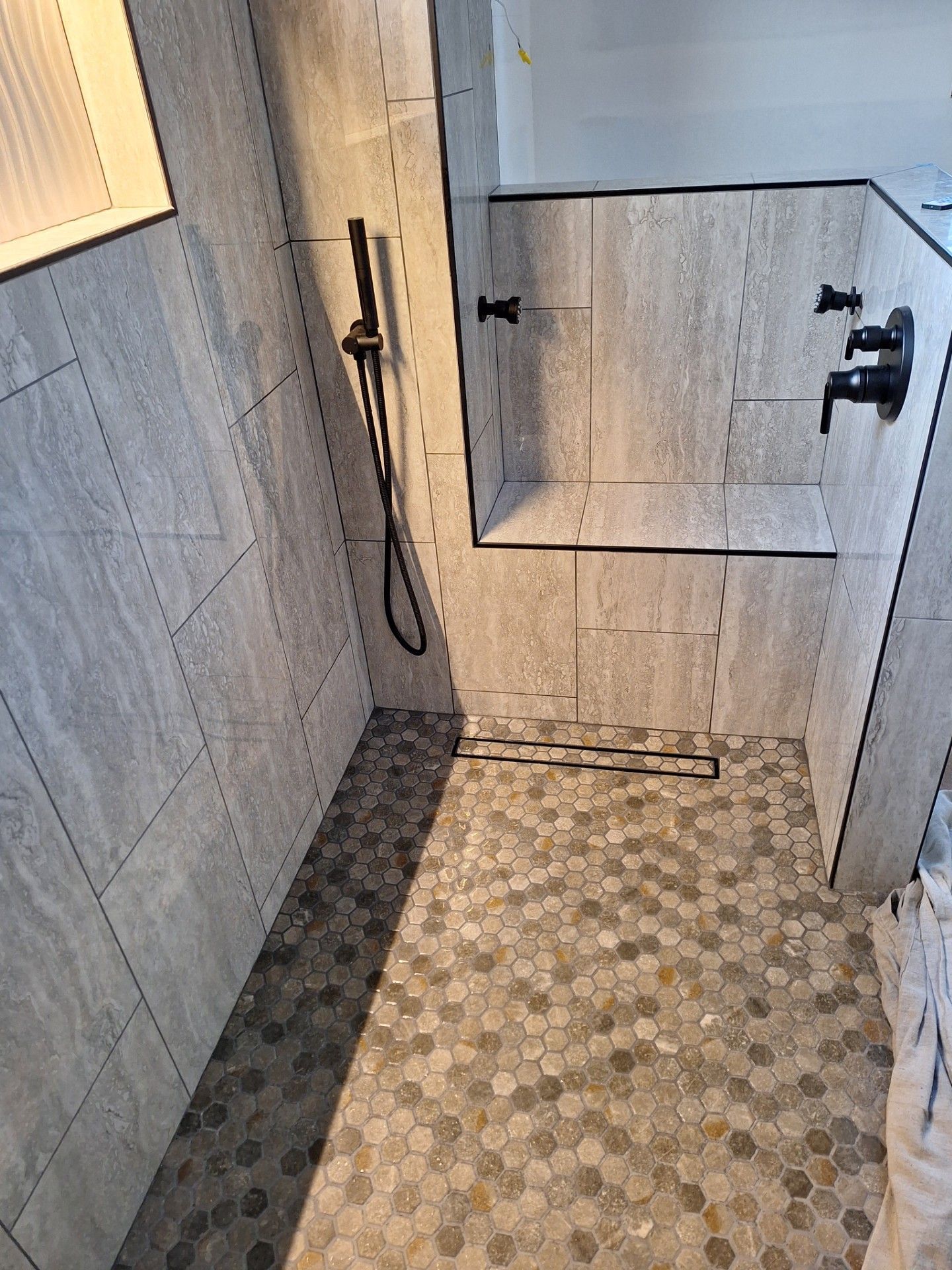 Tile installation process: white wall tiles with spacers, over textured gray wall and flooring, partially covered by wood-like planks.