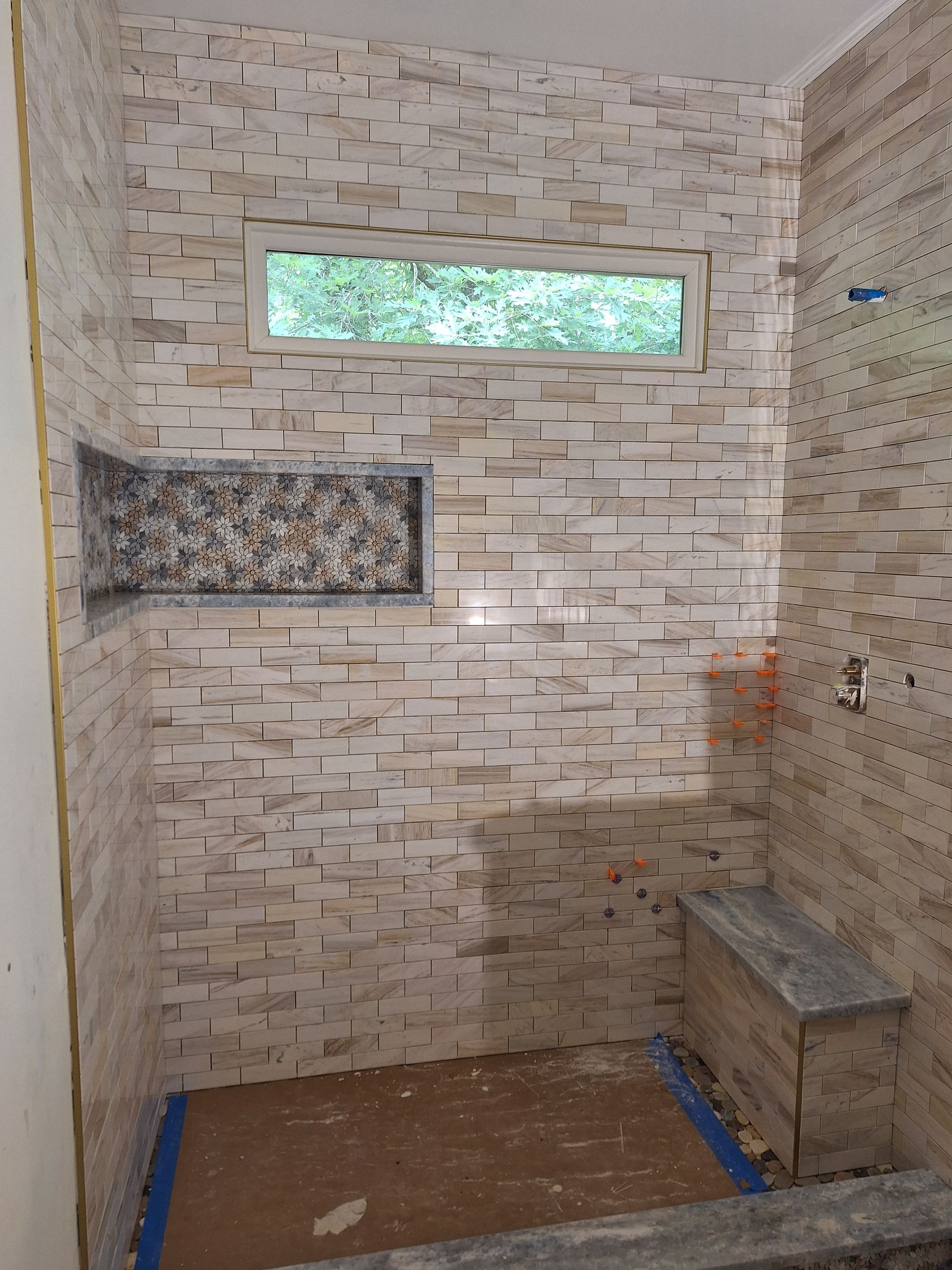 Person installing light-colored flooring with tools: hammer, wrench, level, and utility knife.