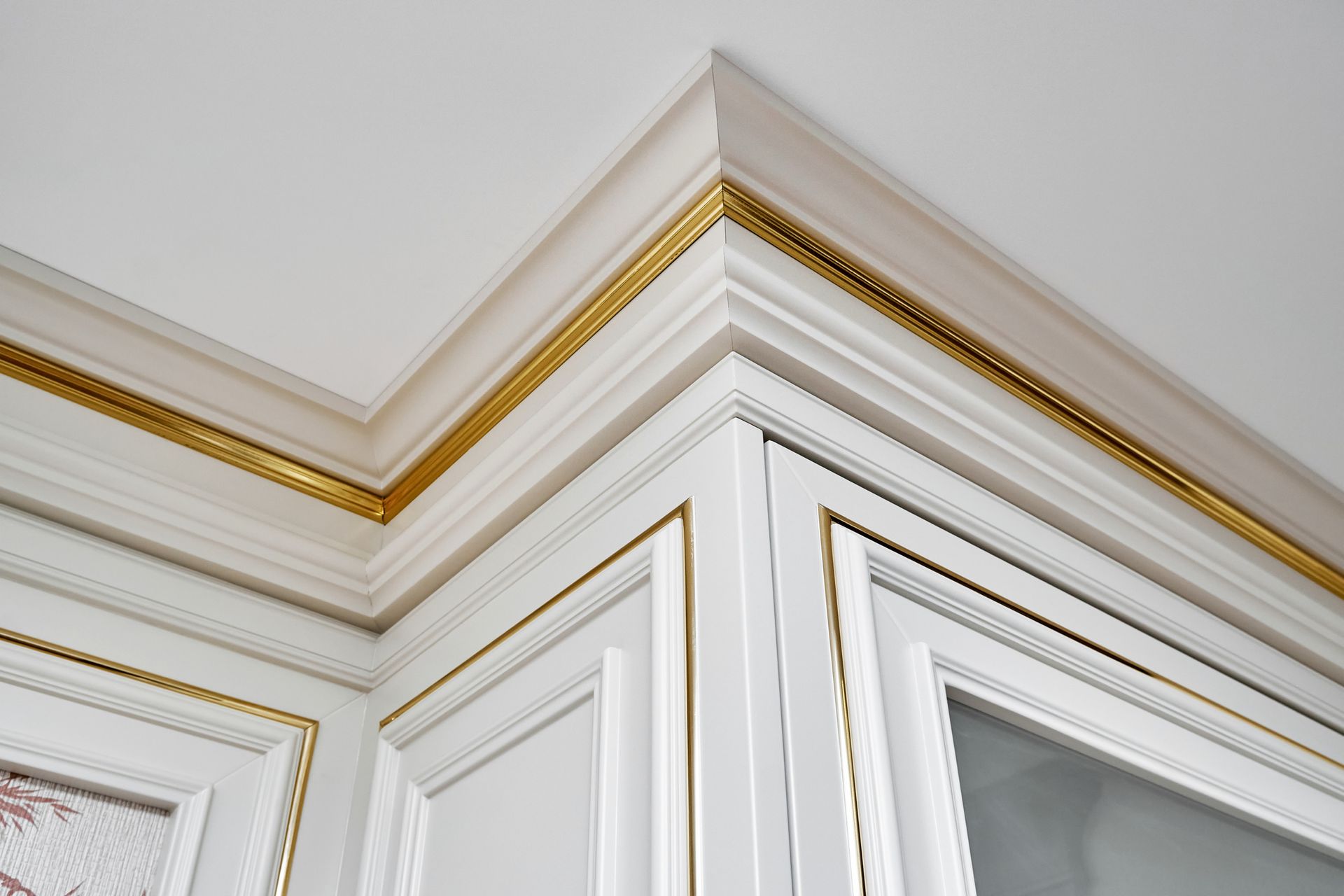 White and gold trim corner on a cabinet with a glass door, in a well-lit room.
