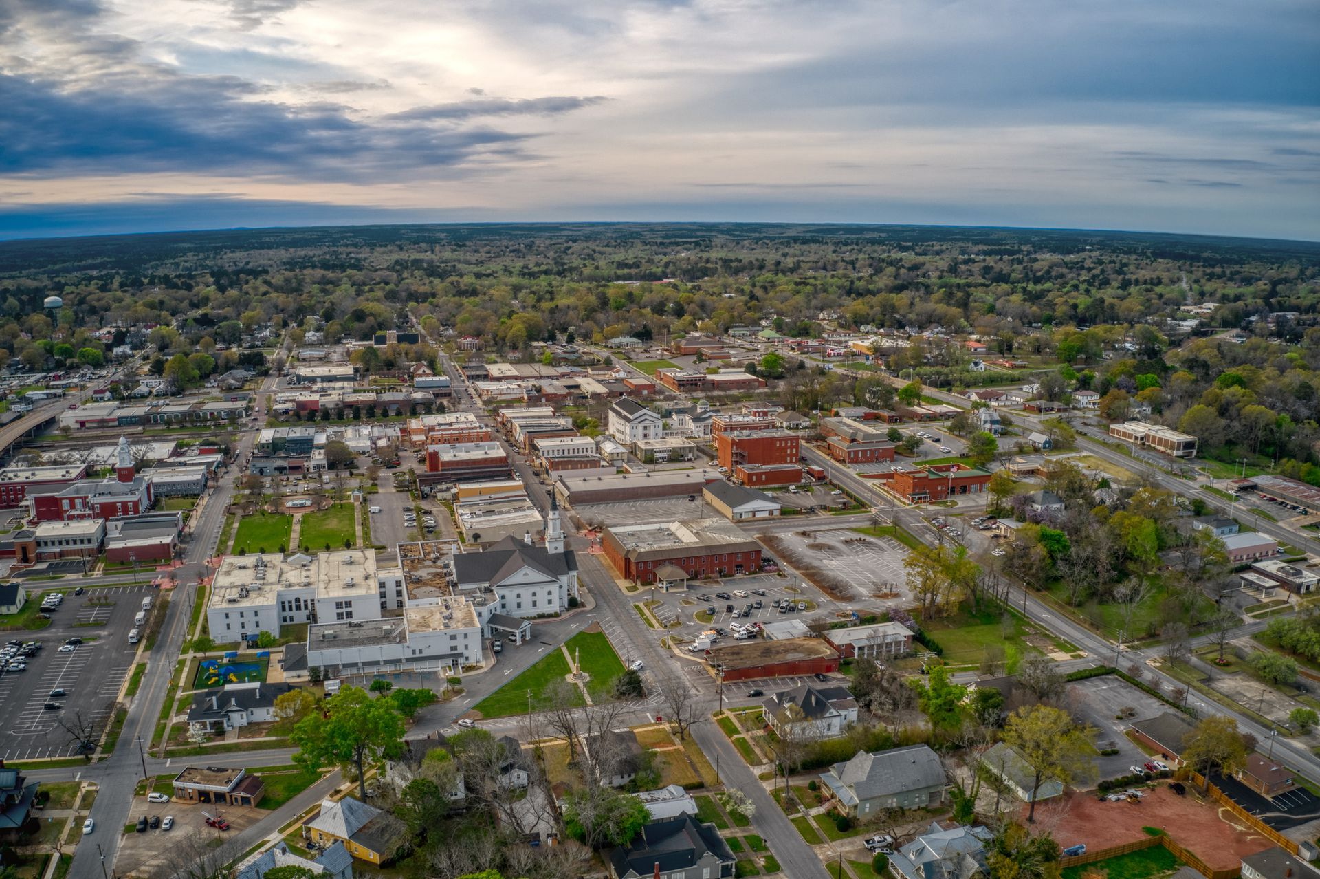 Aerial view of a town with buildings, streets, and trees under a cloudy sky.