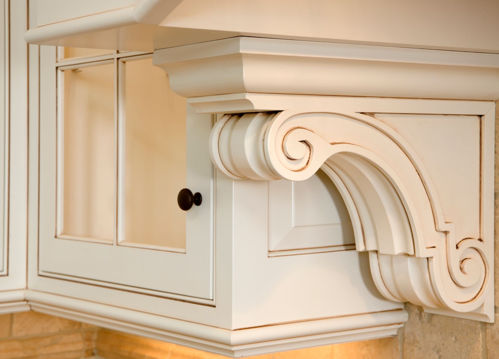 Cream-colored ornate kitchen cabinet with decorative scrollwork and a black knob.