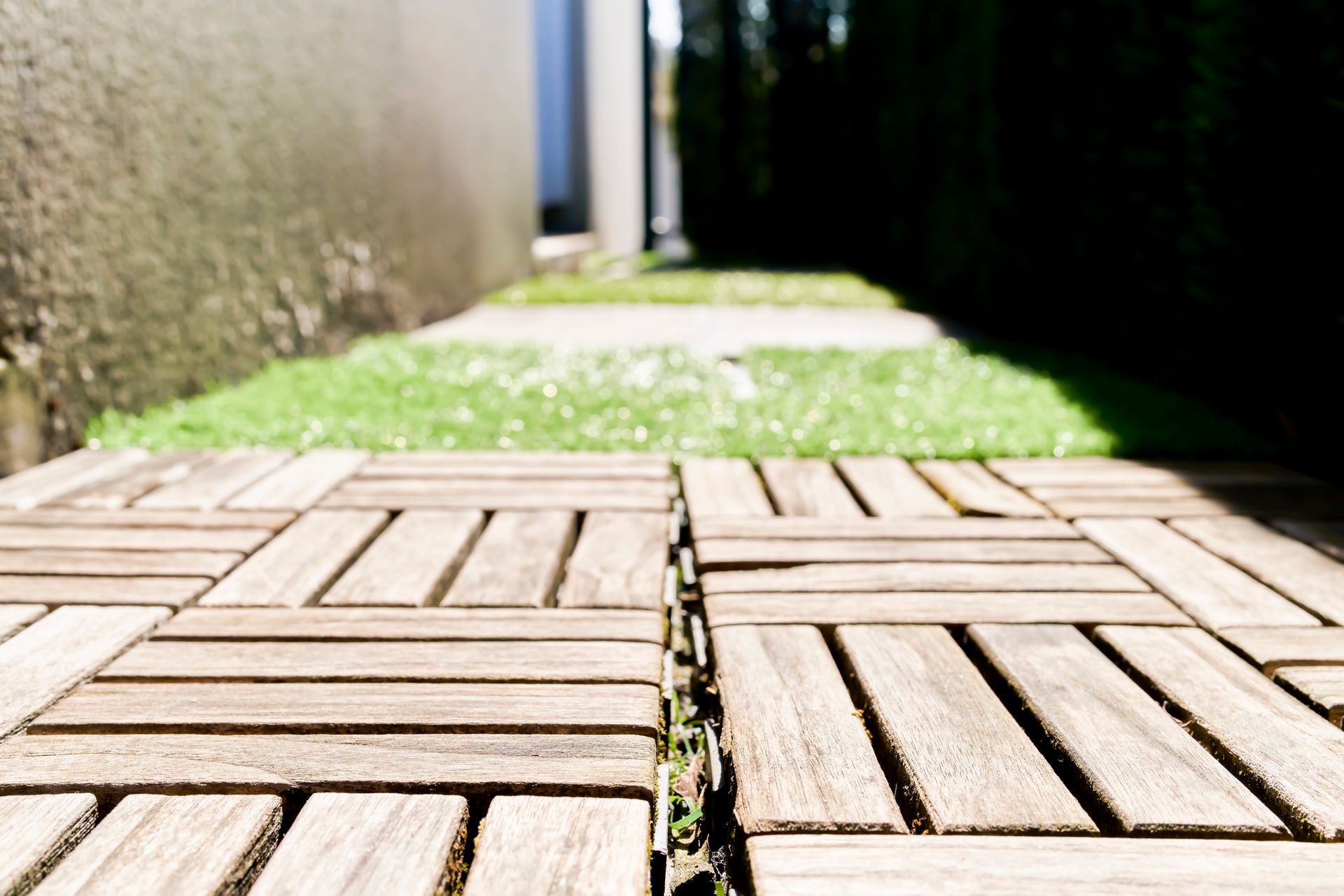 Wooden pathway leading towards green grass and a building on a sunny day.