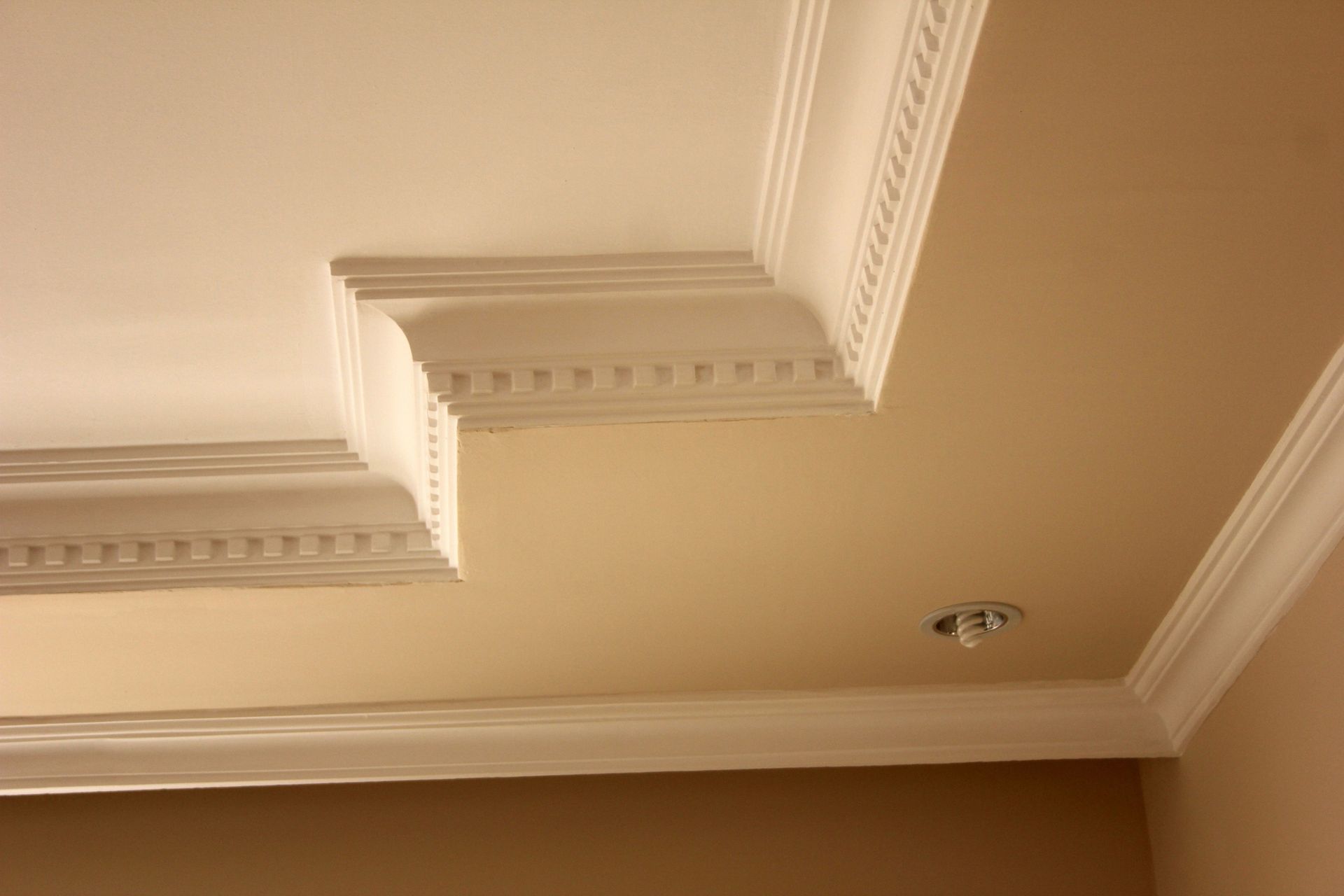 White crown molding around a beige and white ceiling, with a recessed light fixture.
