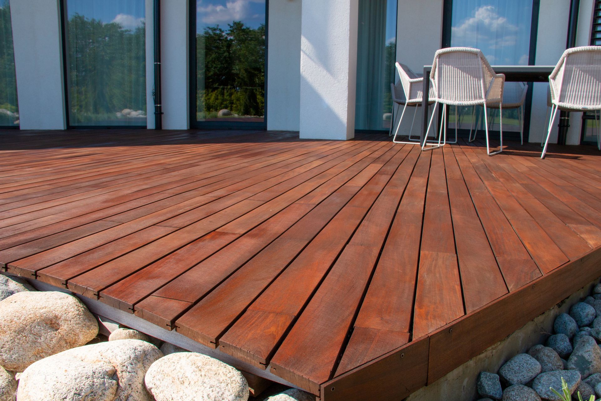 Wooden deck with chairs and table next to a building, surrounded by stones.