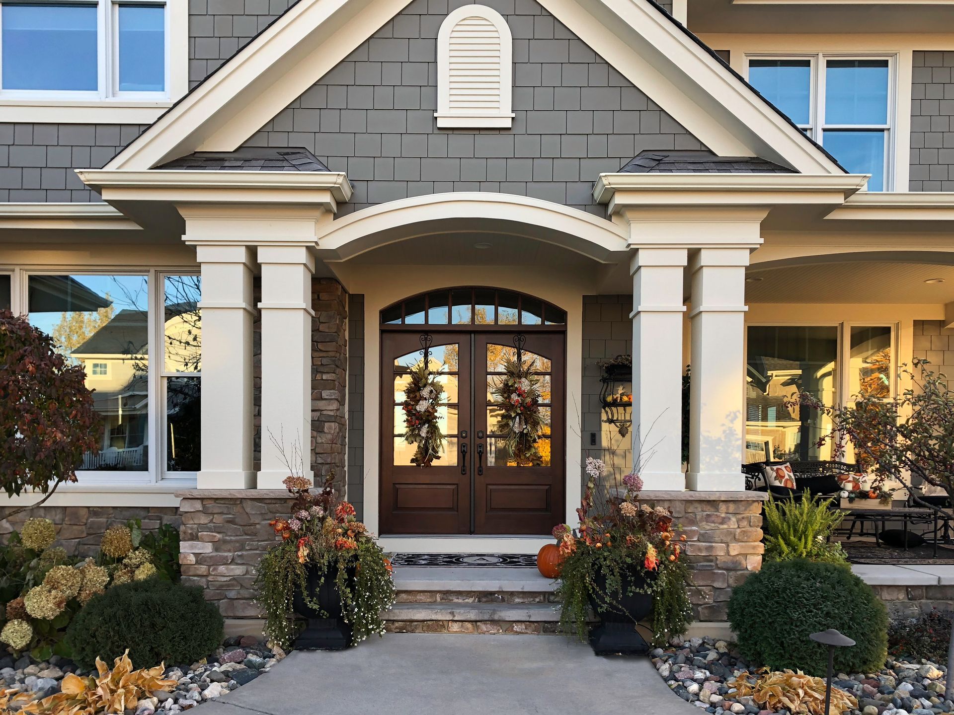 Front entry of a home with double doors, columns, and seasonal decorations; gray siding, beige trim.