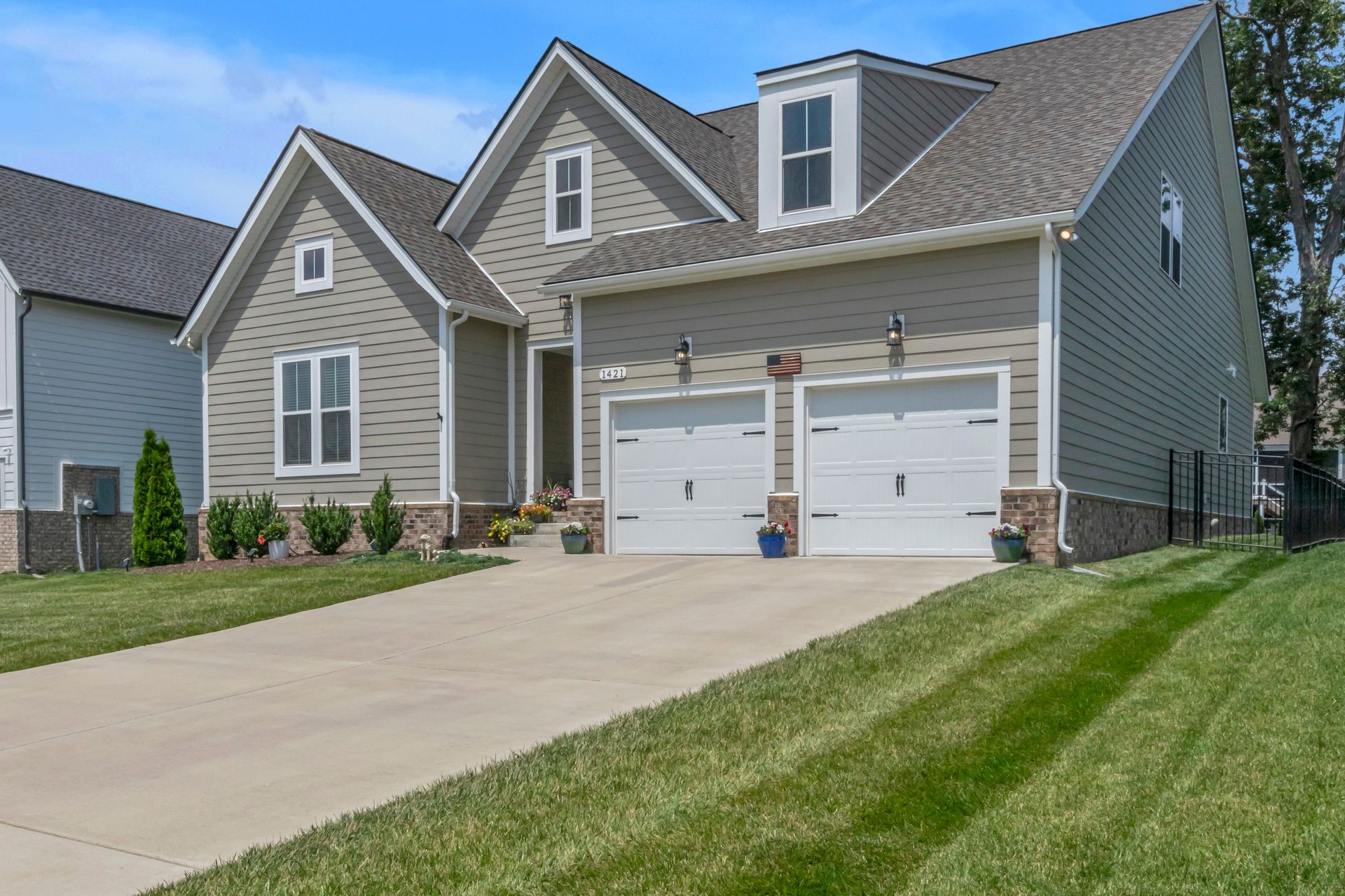 Gray house with white garage doors, driveway, and green lawn.