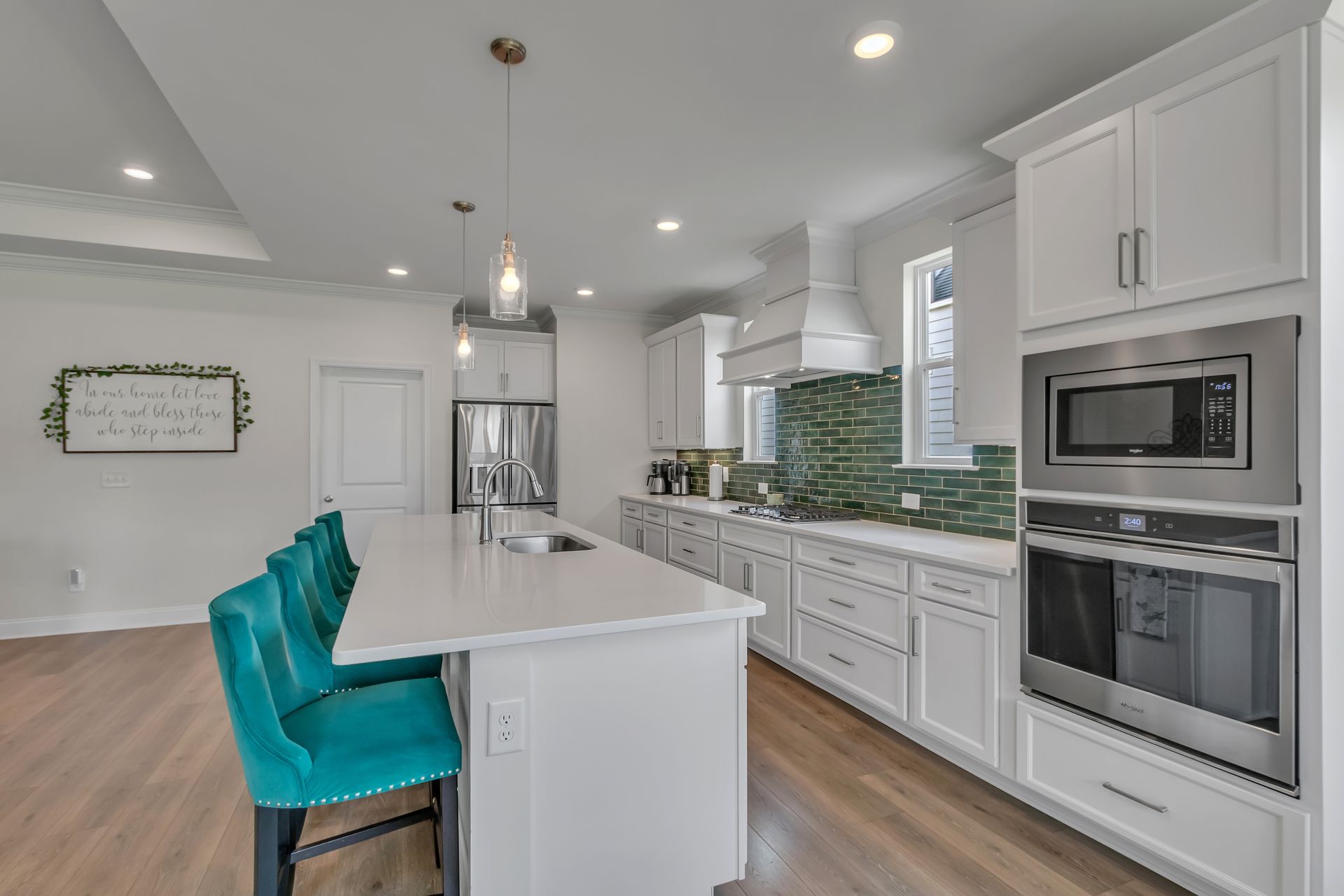 Modern white kitchen with teal accents; island with teal chairs, white cabinets, and green tile backsplash.