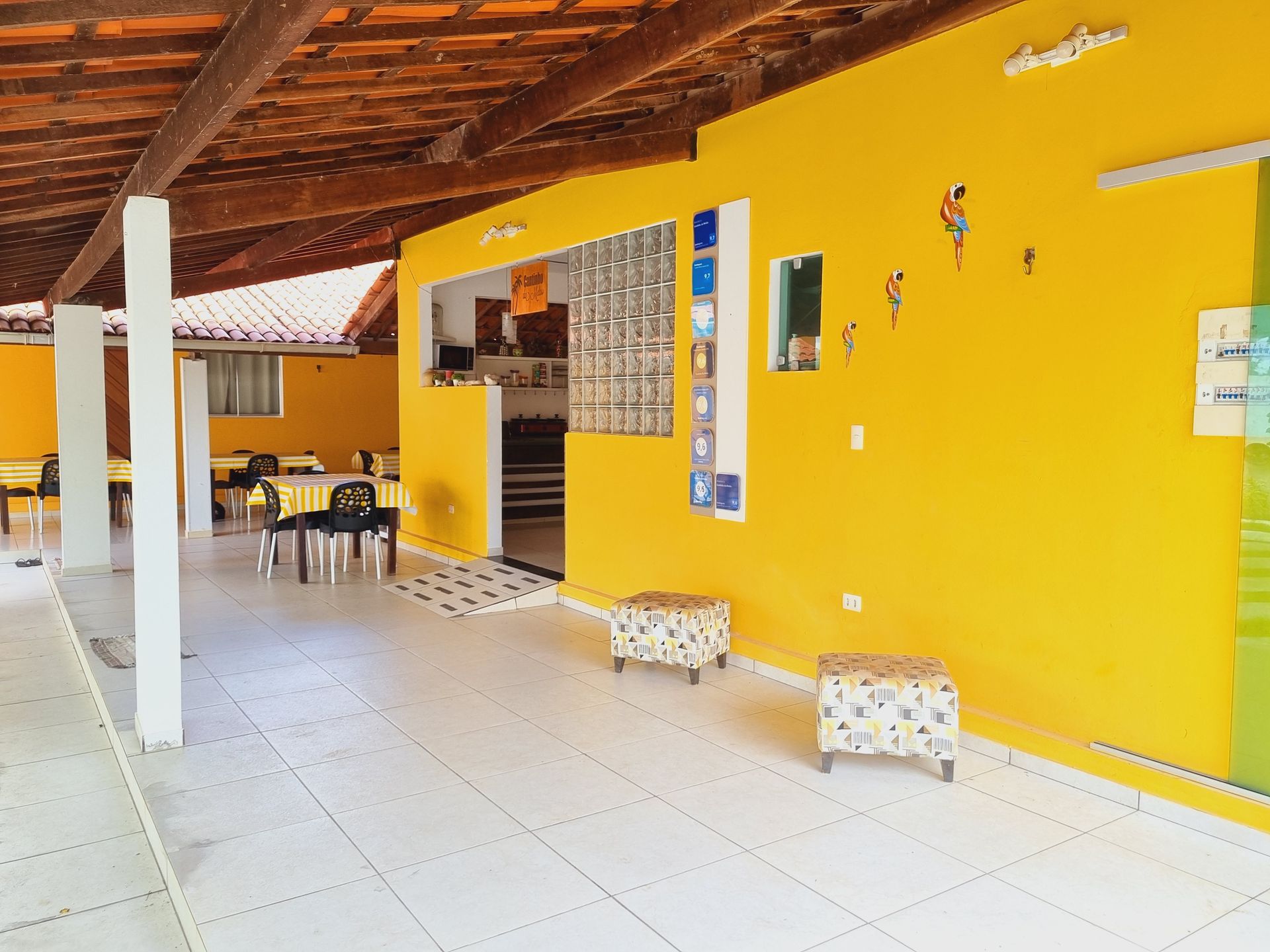 Uma sala com uma parede amarela e piso de ladrilho branco. Pousada Cantinho da Melão