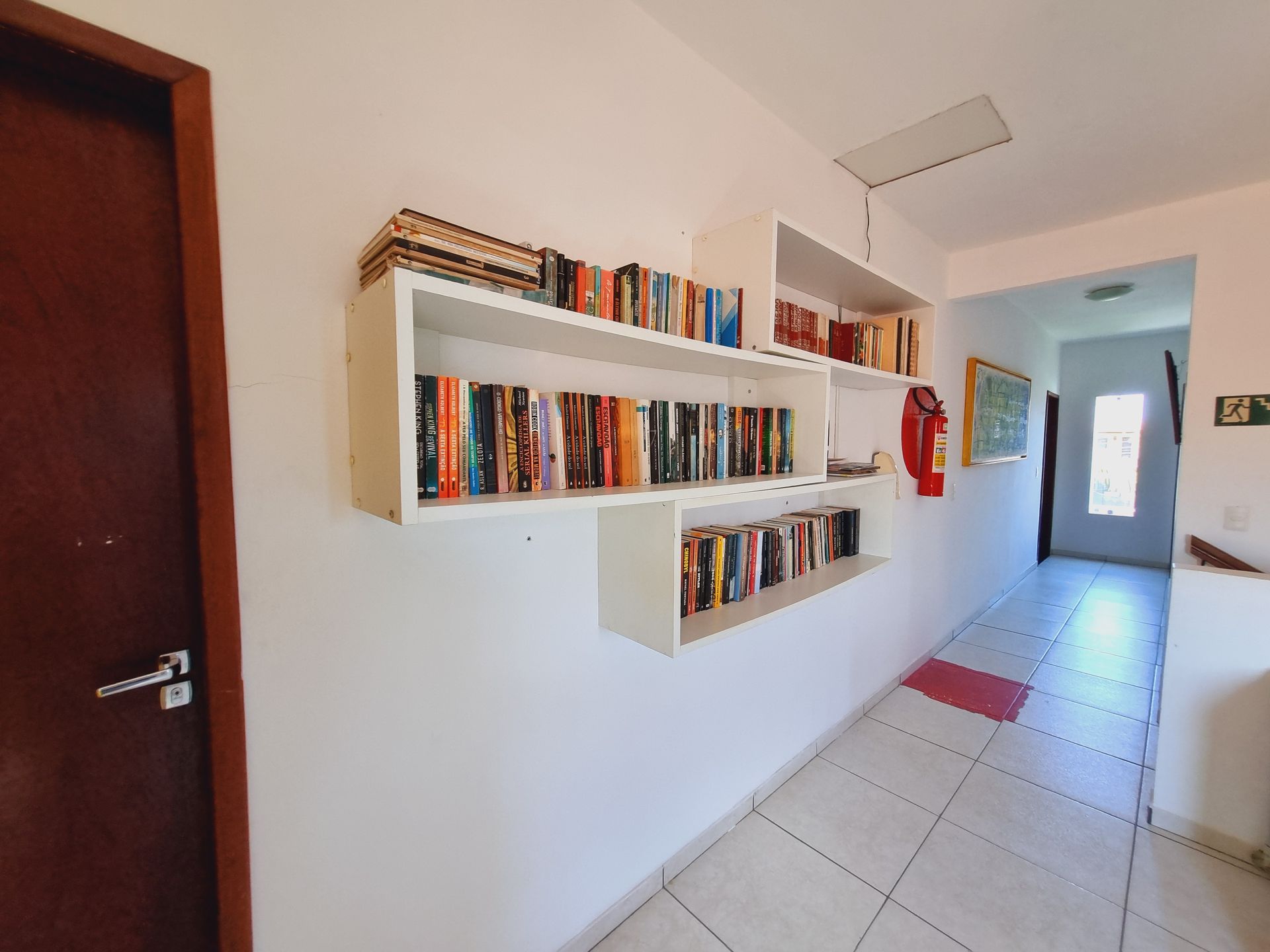 Um corredor com uma estante cheia de livros na parede. Pousada Cantinho da Melão