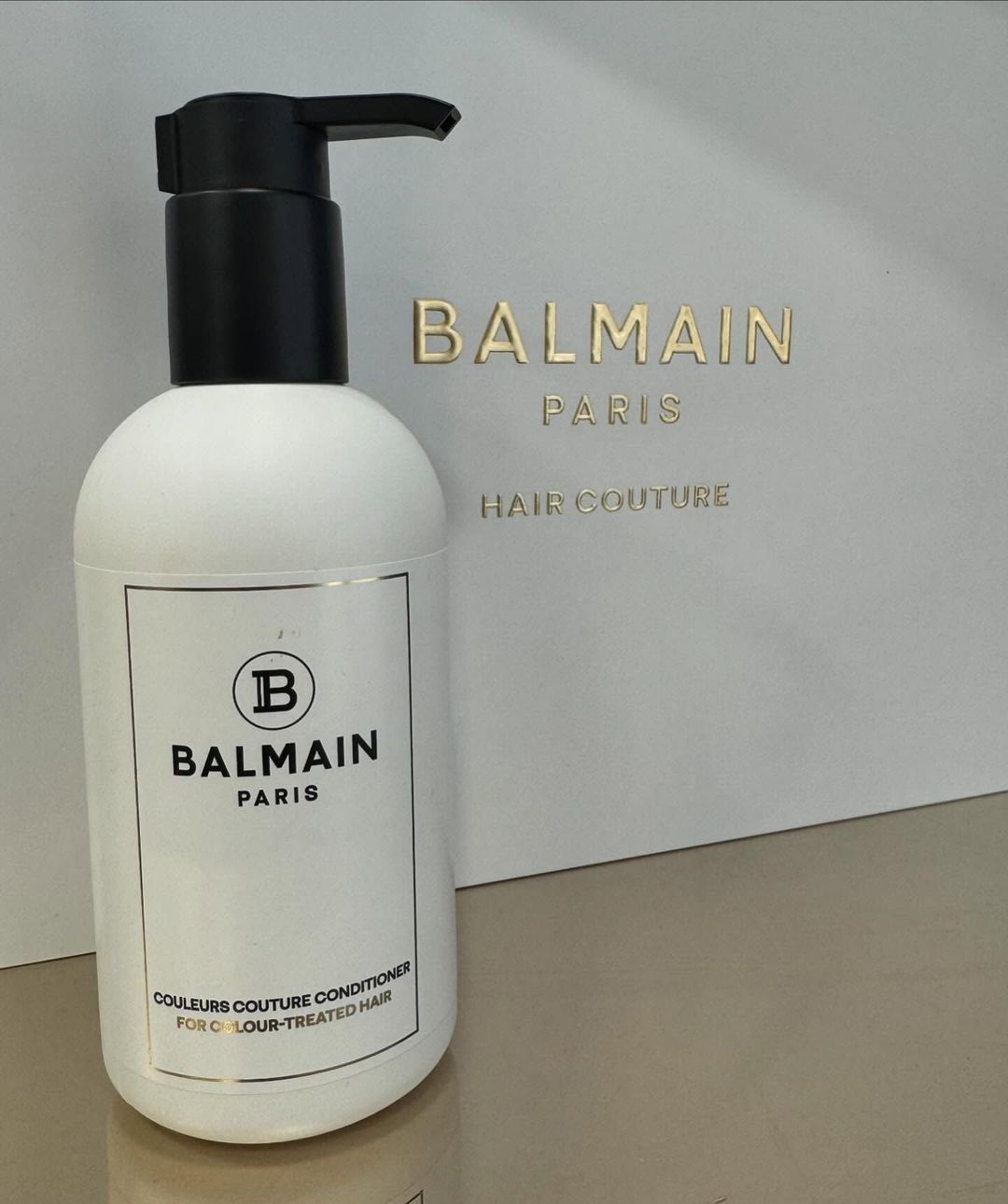 Una bottiglia di balsamo per capelli Balmain è appoggiata su un tavolo accanto a una scatola.