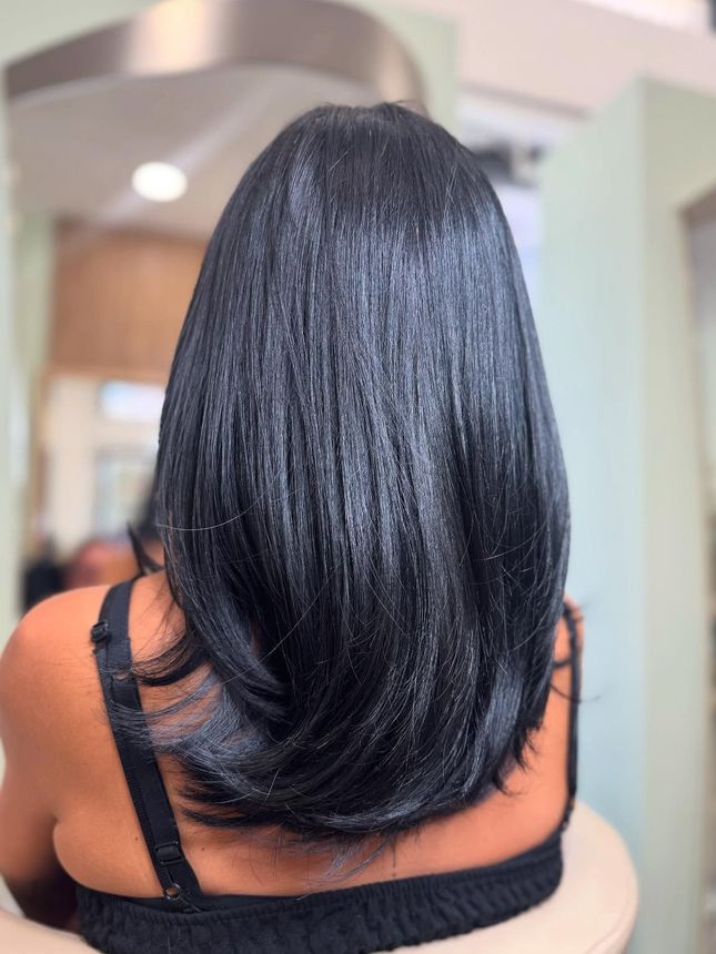 Una donna con lunghi capelli neri è seduta su una sedia davanti a uno specchio.
