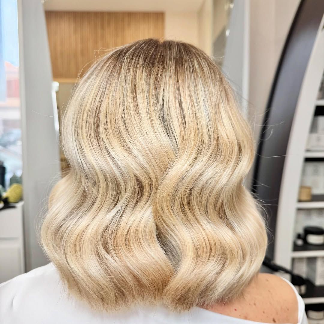 Una donna con i capelli biondi e ondulati è seduta su una sedia in un salone.