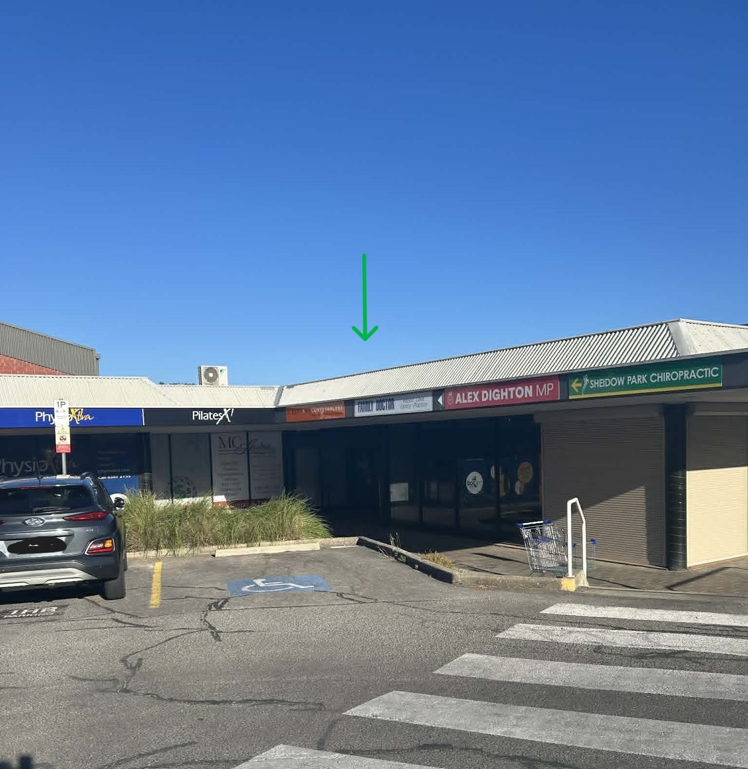 Exterior of a small shopping center on a sunny day; green arrow points to a storefront.