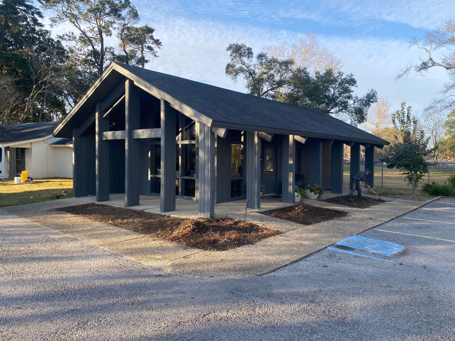 A small house with a gray roof is sitting in the middle of a gravel driveway.