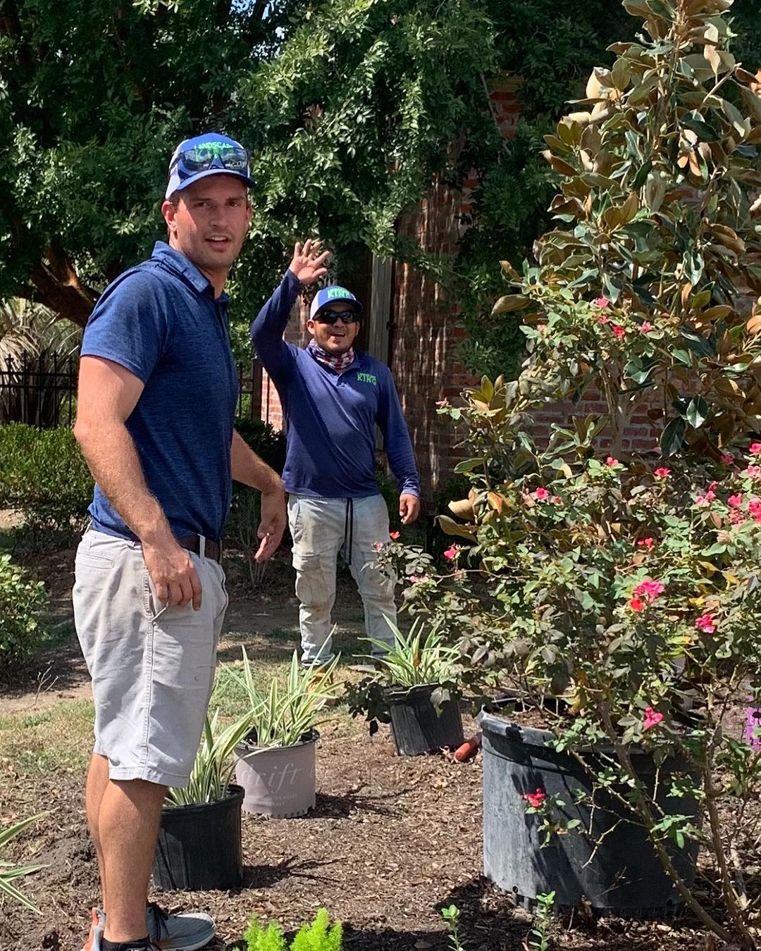 Two men are standing in a garden with potted plants.