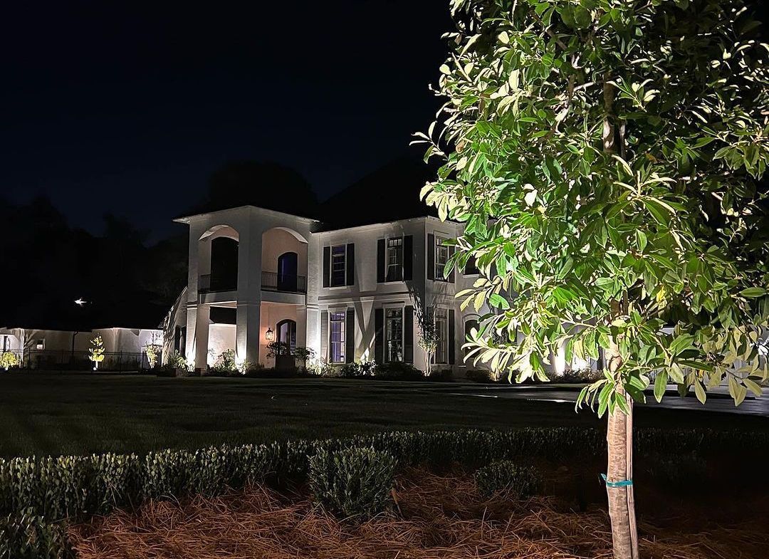 A large house is lit up at night with a tree in front of it.