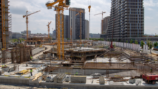 A large construction site with a lot of cranes and buildings in the background.