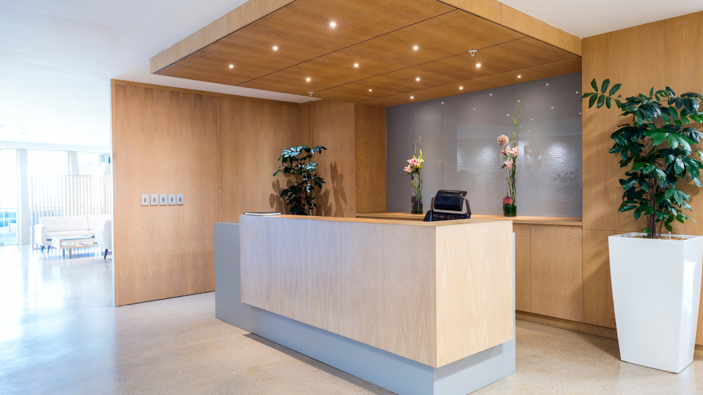 A hotel lobby with a wooden reception desk and a potted plant.