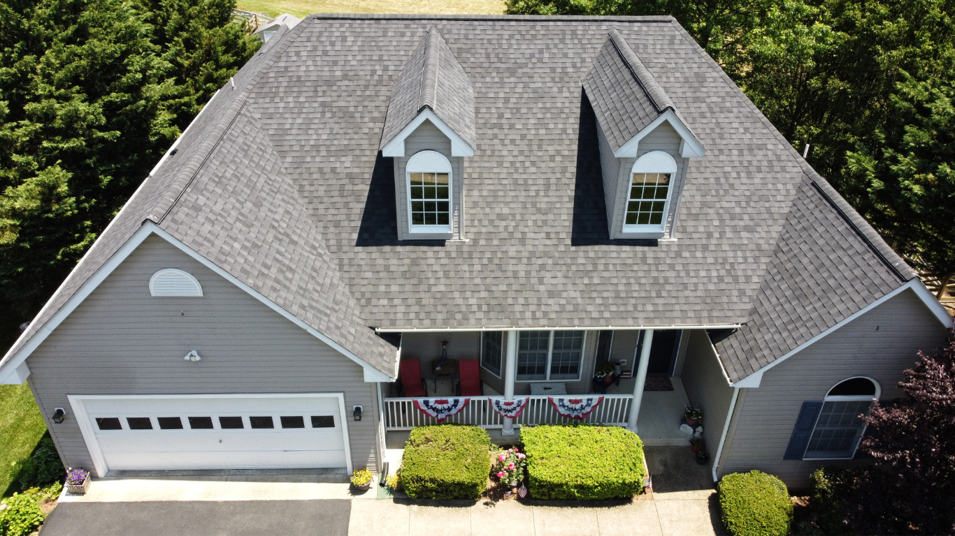 An aerial view of a large house with a gray roof surrounded by trees.