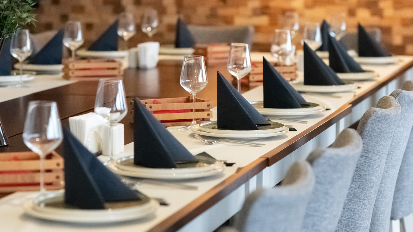 A long table with plates , napkins , glasses and utensils on it.