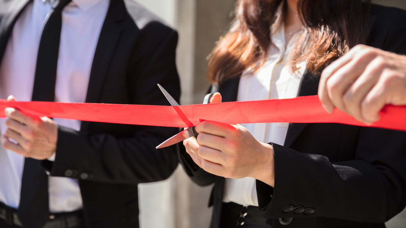 A man and a woman are cutting a red ribbon with scissors.