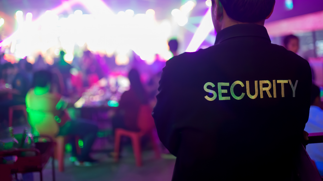 A security guard is standing in front of a crowd of people at a party.