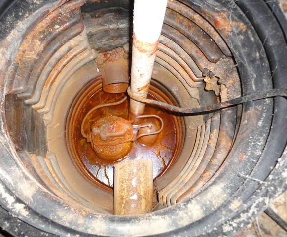 Rusty sump pump components inside a dark plastic pit.