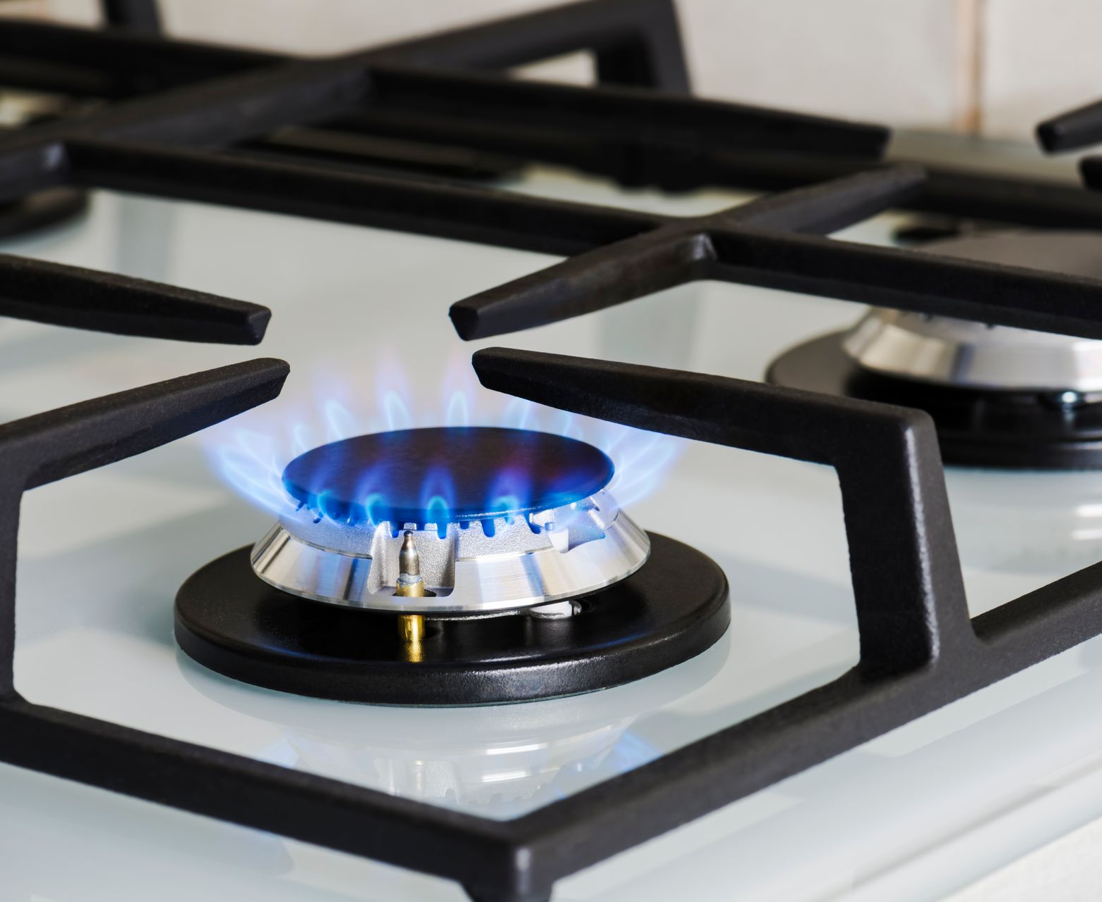 Gas stove burner lit with blue flames, black grates, white surface.