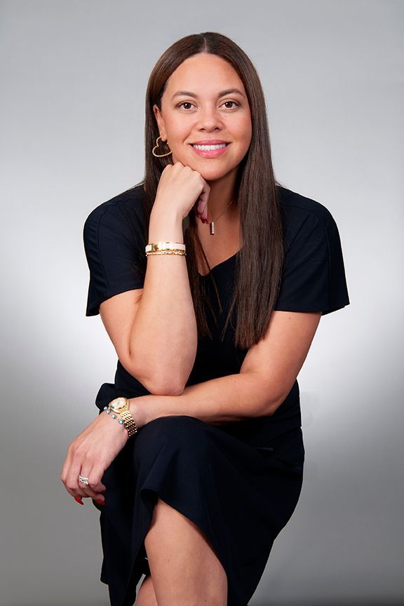 A woman is sitting at a desk with a laptop and a vase of flowers.