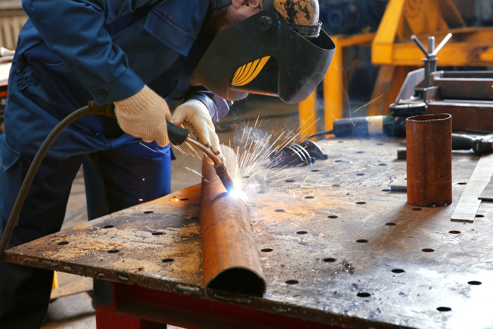 Welder using welding equipment for metalworking in shop.