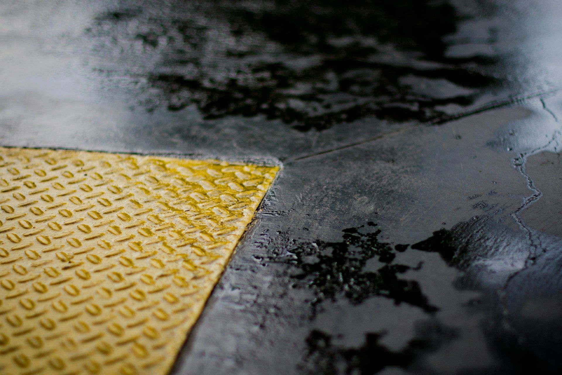 Wet black pavement with a yellow textured tactile curb ramp edge