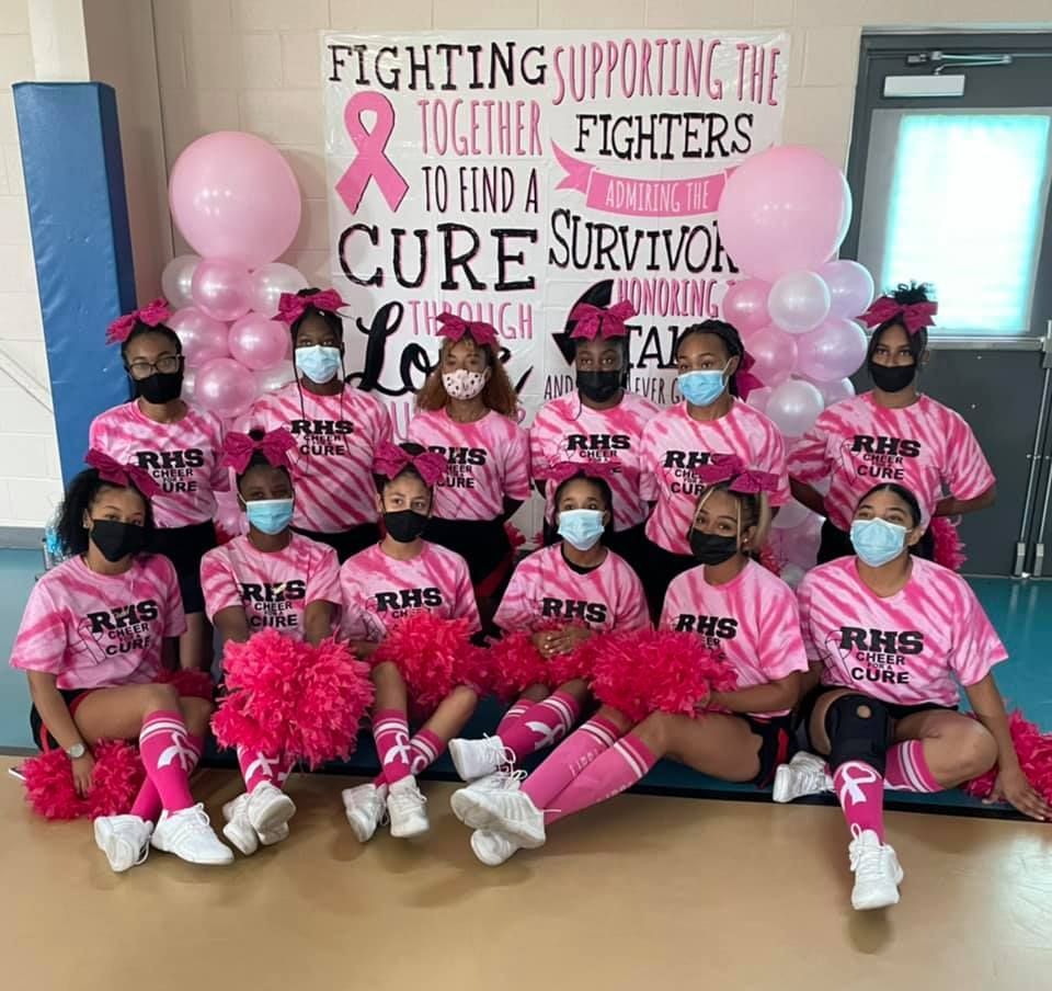 Cheerleaders in pink for breast cancer awareness, with balloons and banner.