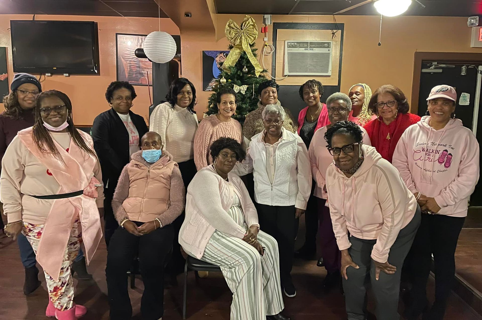 Group of women in pink posing indoors by a Christmas tree.
