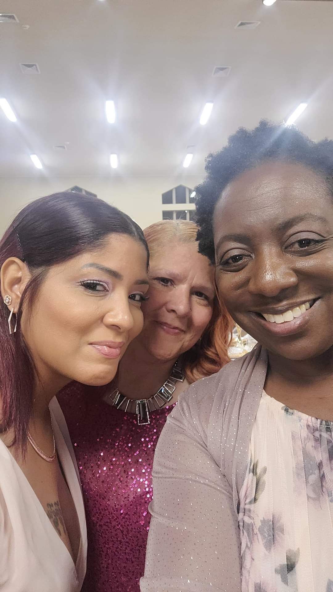 Three women smile at the camera. One with curly black hair, one with reddish hair, and one with long brown hair.