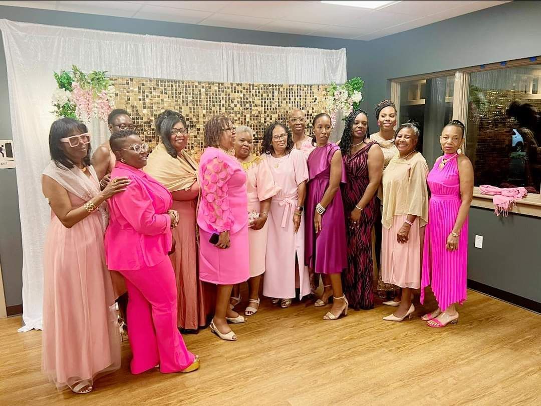 Group of women in shades of pink posing in front of a decorated wall.