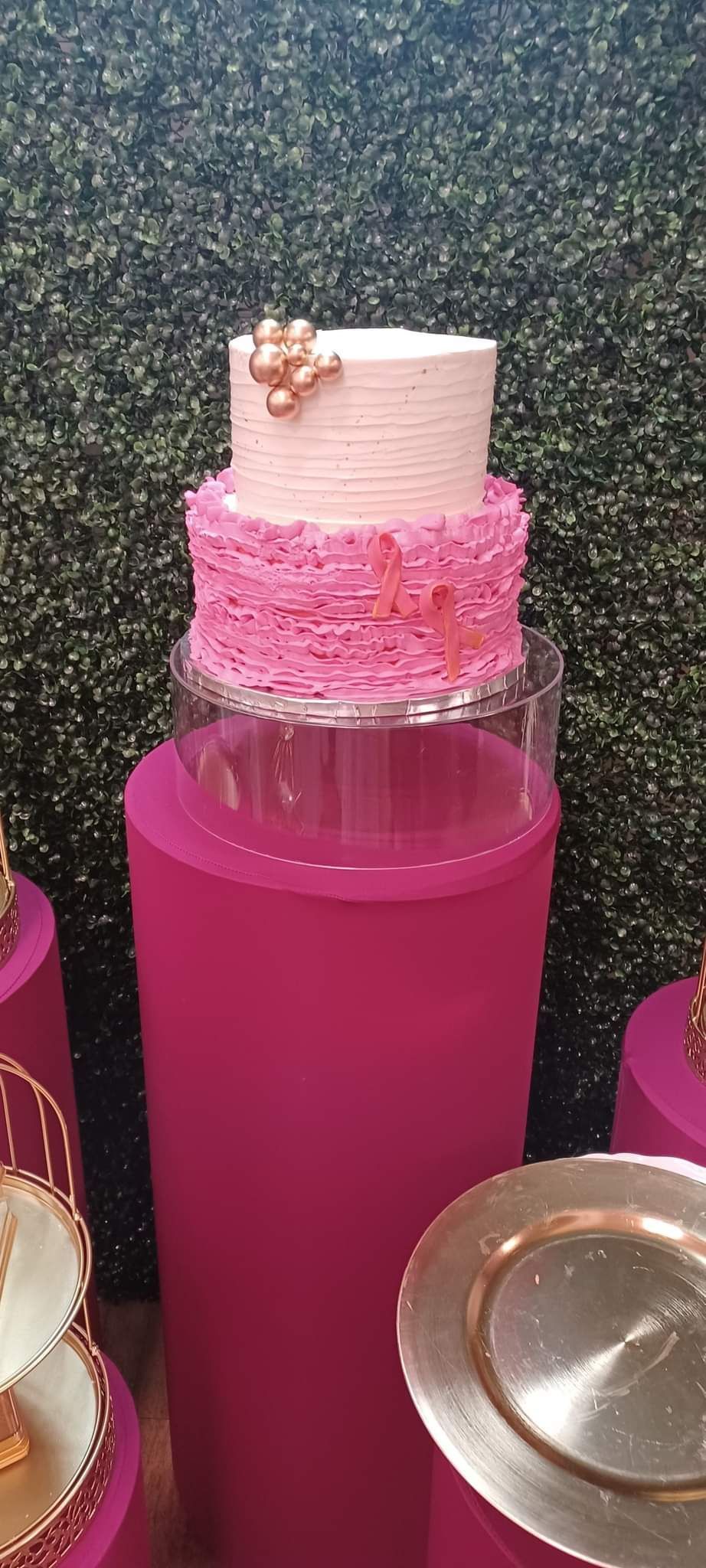 Three-tiered pink cake on a magenta pedestal. Gold bow, against a dark green backdrop.
