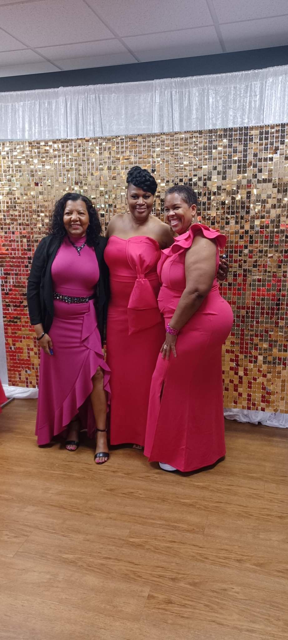 Three women in pink dresses posing in front of a gold sequin wall.