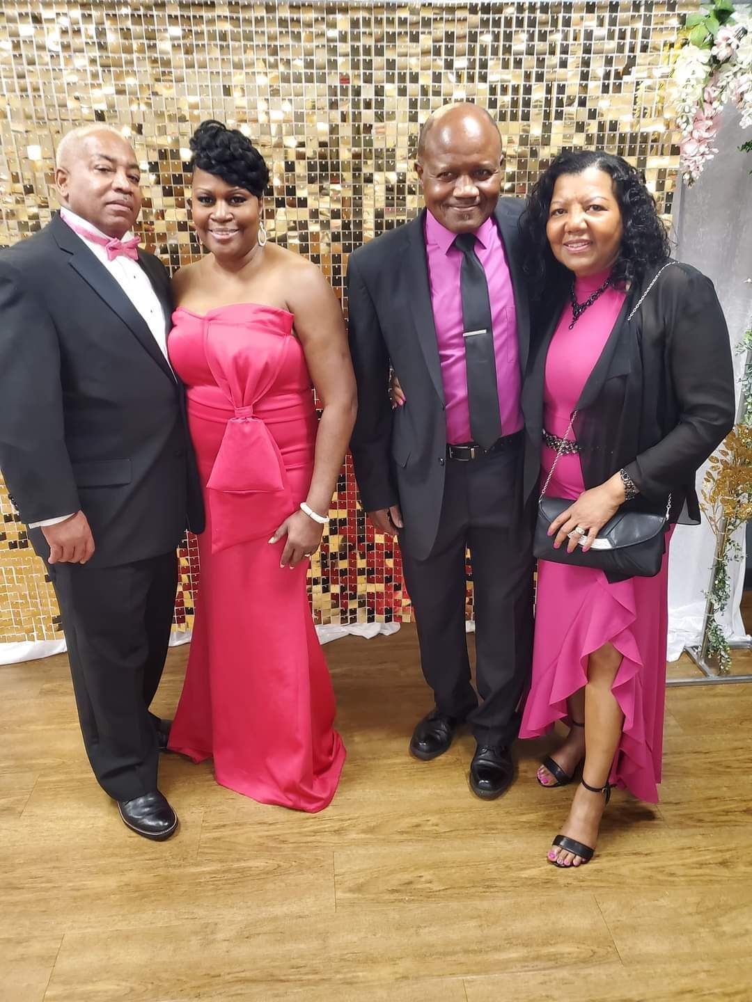 Four people dressed in formal attire pose for a photo in front of a gold sequin backdrop.