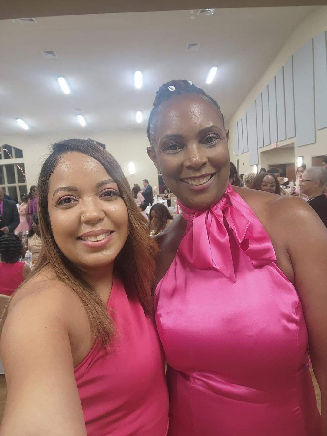Two women in pink dresses smiling at a gala event.
