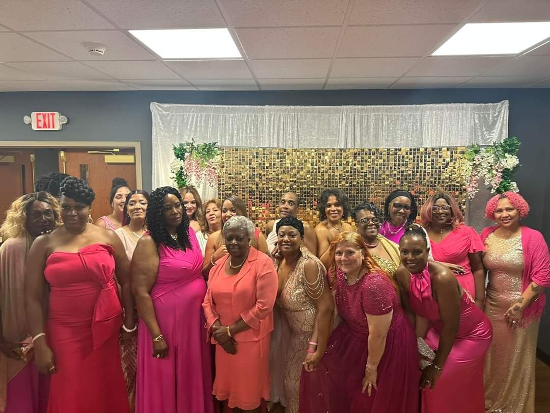 Group of women in pink and peach dresses posing for a photo at an event, possibly a party.