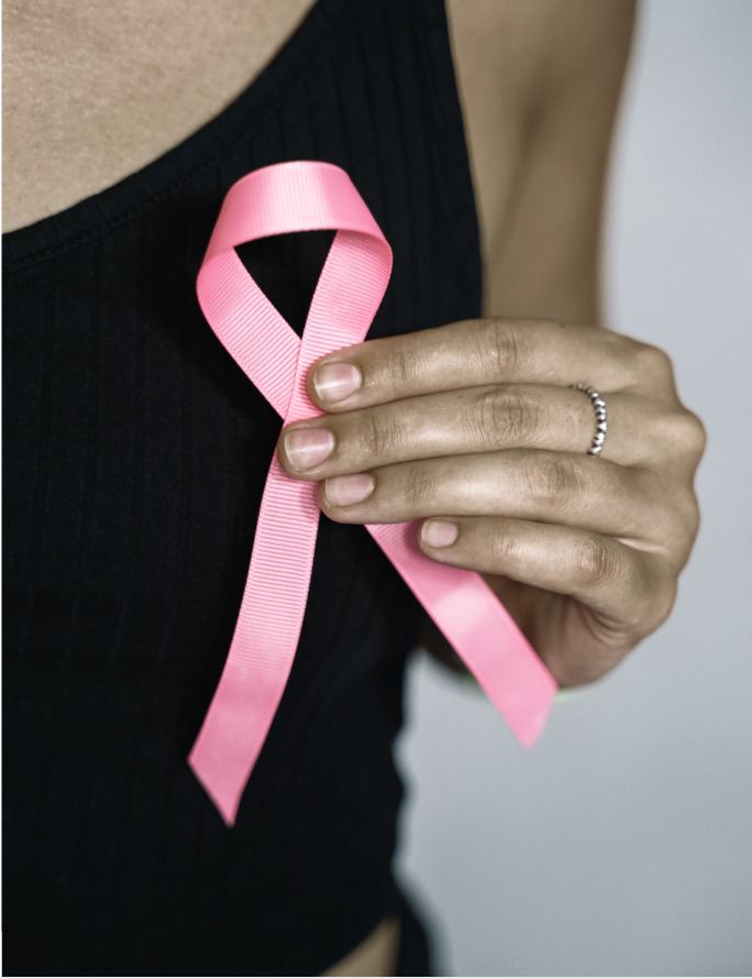 Woman holding a pink ribbon on her chest, symbolizing breast cancer awareness.