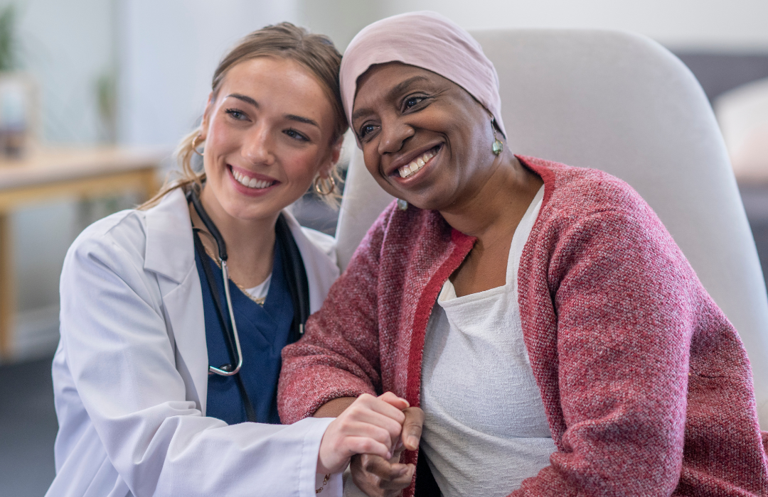 A doctor in a white coat smiles with a woman wearing a headscarf, both holding hands.