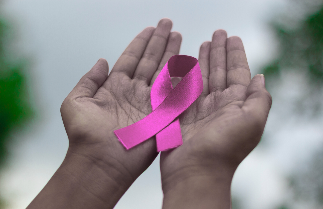Hands cupping a pink ribbon, symbolizing breast cancer awareness.