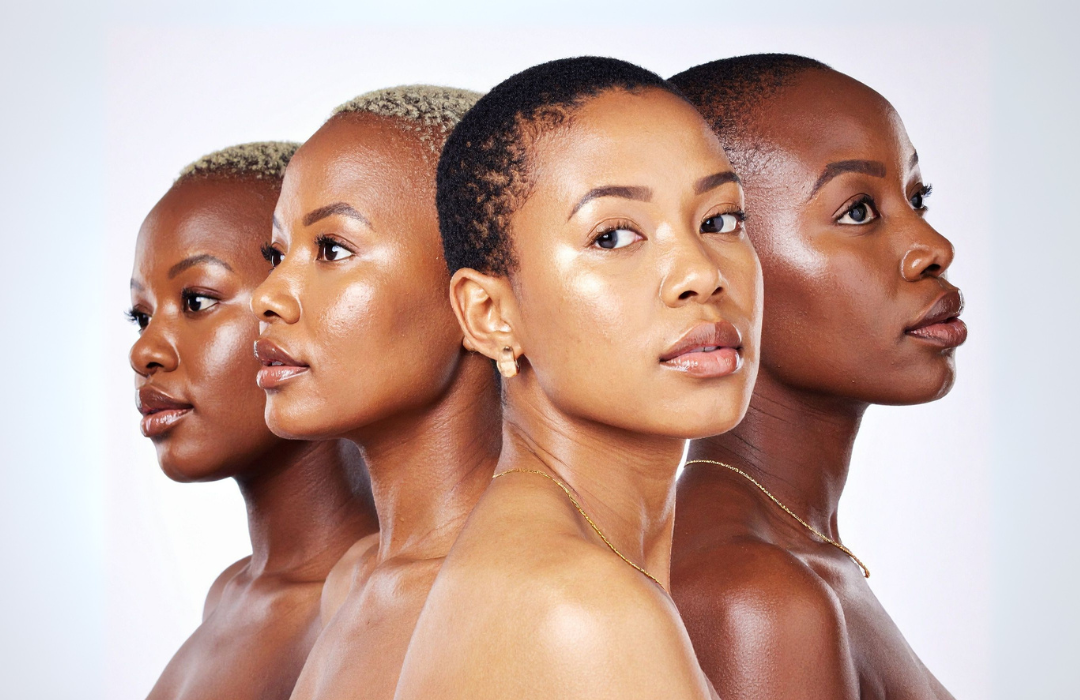Four diverse women with glowing skin stand in a row against a white backdrop, looking thoughtful.