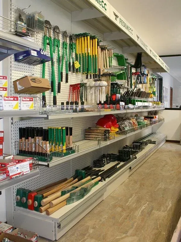 Scaffali pieni di attrezzi verdi e gialli, tra cui martelli e cesoie, in un negozio di ferramenta.