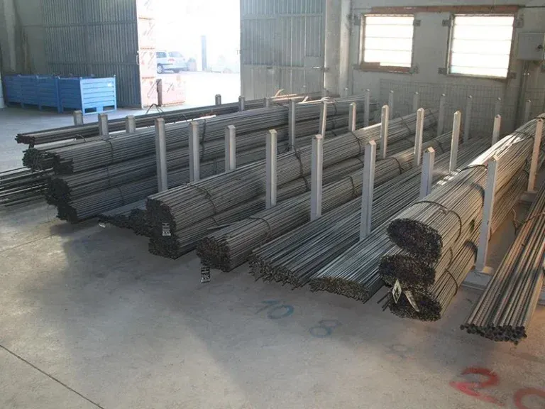 Fasci di barre d'acciaio immagazzinati su scaffalature all'interno di un magazzino.