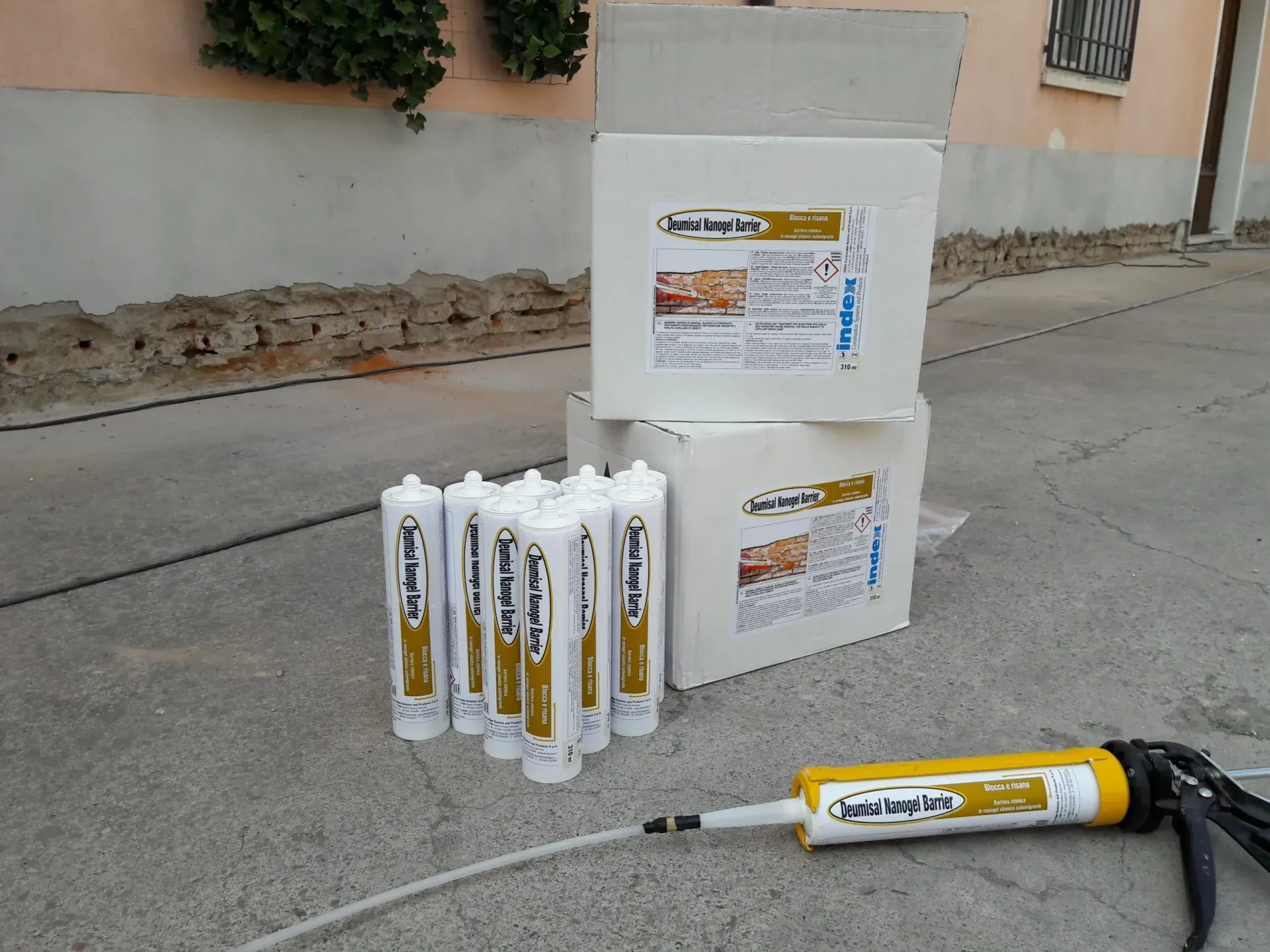 Scatole bianche e tubetti di sigillante con una pistola per calafataggio gialla su una superficie di cemento.